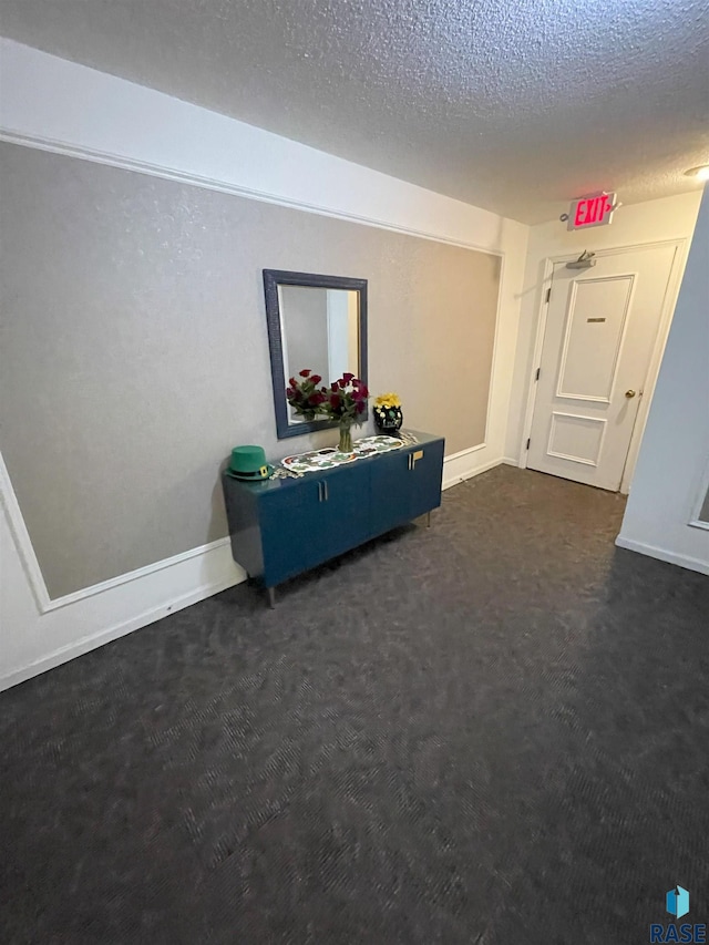 interior space with dark colored carpet, a textured ceiling, and baseboards