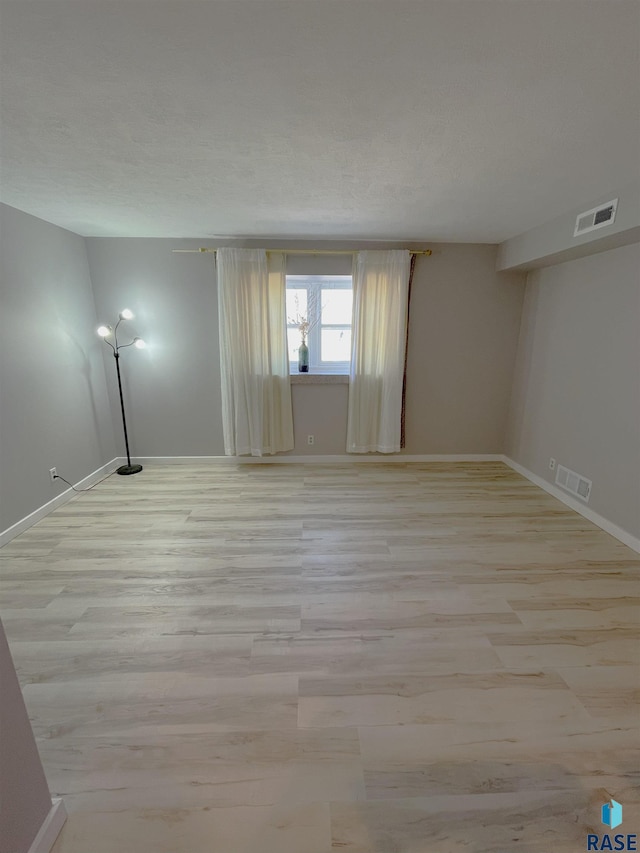 unfurnished room featuring light wood-type flooring, visible vents, and baseboards