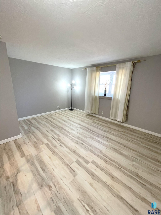 empty room featuring light wood-type flooring, baseboards, and a textured ceiling