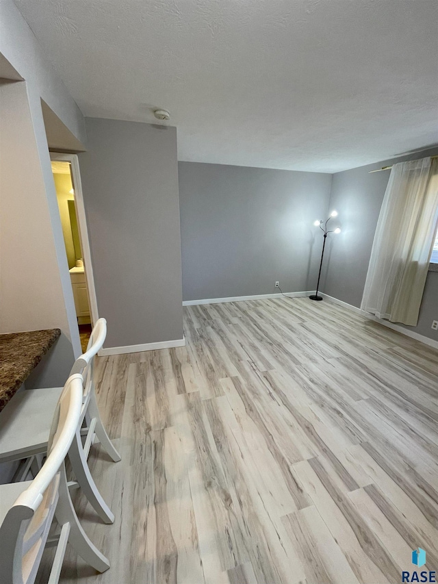 empty room with a textured ceiling, light wood-style flooring, and baseboards