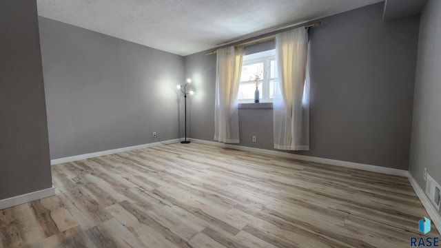 spare room with light wood-style floors, visible vents, and baseboards