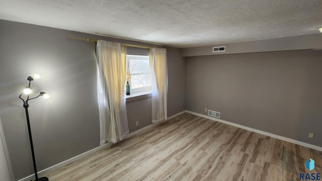 unfurnished room with light wood-style flooring, visible vents, and a textured ceiling