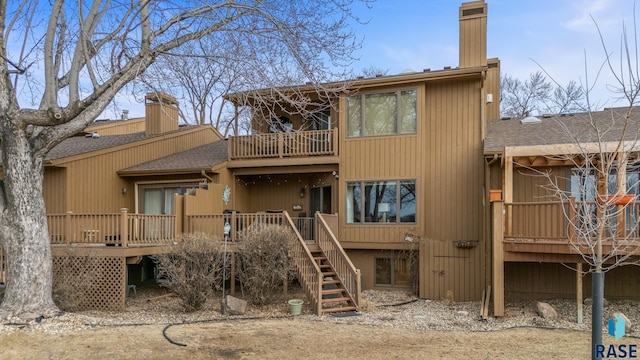 rear view of property with roof with shingles, a chimney, a balcony, a wooden deck, and stairs