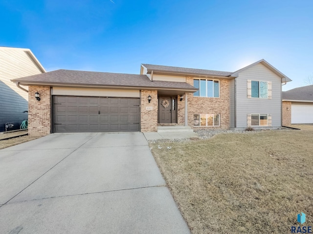 tri-level home with driveway, an attached garage, a front lawn, and brick siding