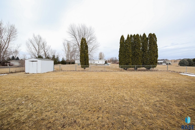 view of yard with a storage unit, a rural view, an outdoor structure, and fence