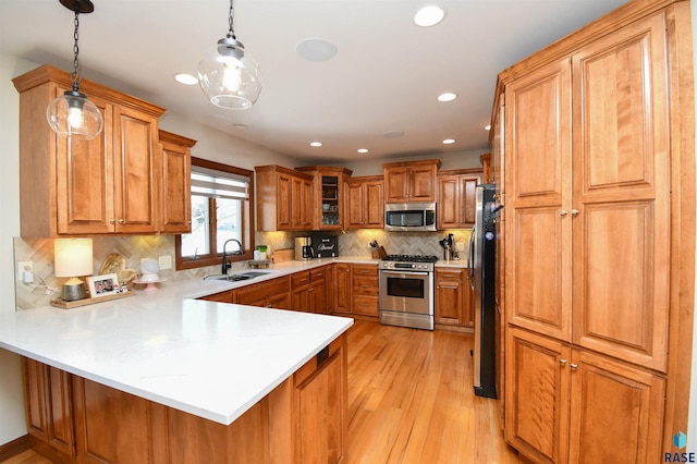 kitchen with a peninsula, a sink, light countertops, appliances with stainless steel finishes, and pendant lighting