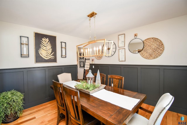 dining space with light wood-style floors, a chandelier, a decorative wall, and wainscoting