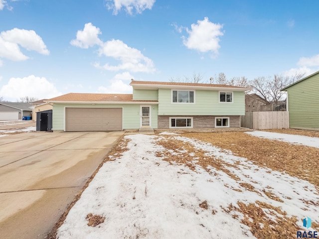 split level home with an attached garage, fence, and concrete driveway