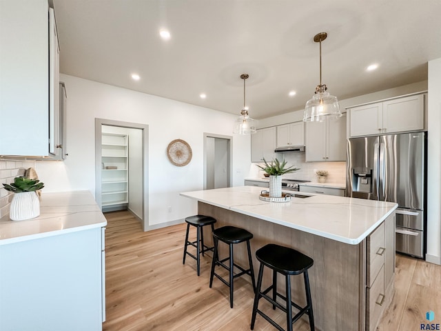 kitchen with decorative backsplash, stainless steel fridge with ice dispenser, a spacious island, light wood-style flooring, and decorative light fixtures