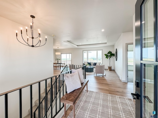 hall featuring baseboards, a raised ceiling, an upstairs landing, light wood-style floors, and recessed lighting