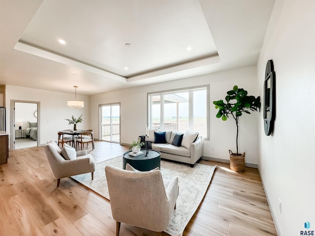 living room featuring light wood-type flooring, a tray ceiling, baseboards, and recessed lighting