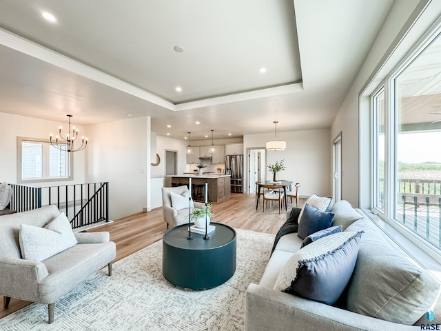 living area with light wood-style floors, a raised ceiling, a notable chandelier, and plenty of natural light