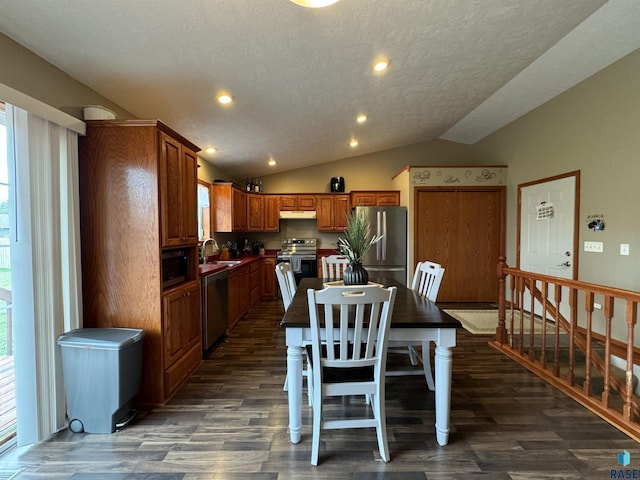 kitchen featuring under cabinet range hood, vaulted ceiling, appliances with stainless steel finishes, brown cabinets, and dark wood finished floors