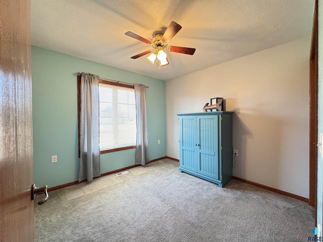 carpeted empty room with a ceiling fan, visible vents, a textured ceiling, and baseboards