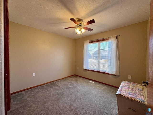 carpeted empty room featuring a ceiling fan, visible vents, a textured ceiling, and baseboards