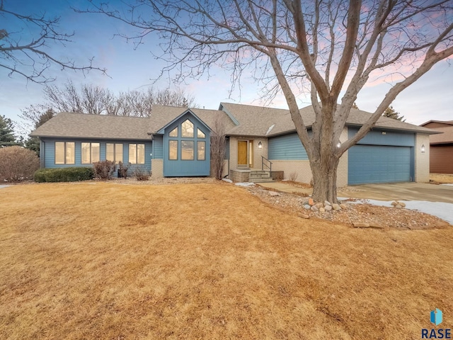 view of front of house with concrete driveway, roof with shingles, an attached garage, a front lawn, and brick siding