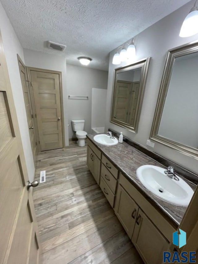 full bathroom with double vanity, visible vents, a sink, and wood finished floors