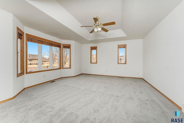 unfurnished room with a ceiling fan, a tray ceiling, light colored carpet, and baseboards