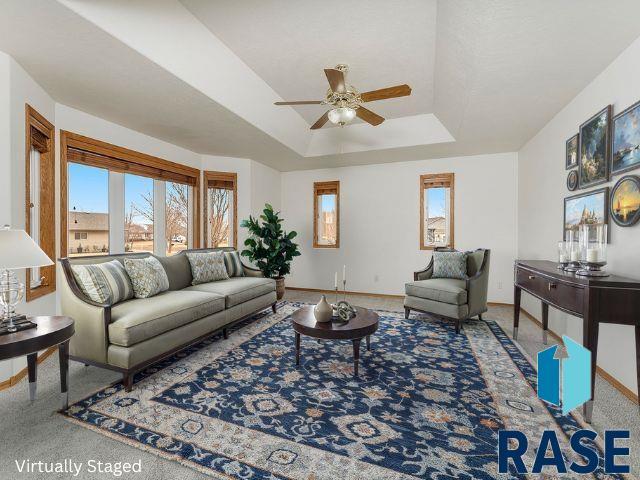 living area featuring ceiling fan, baseboards, and a raised ceiling