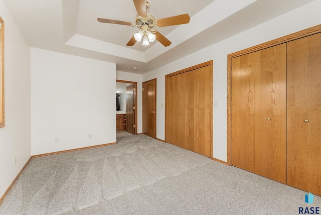 unfurnished bedroom featuring baseboards, a raised ceiling, connected bathroom, light colored carpet, and multiple closets