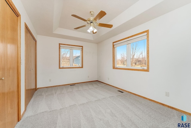 unfurnished bedroom featuring light carpet, multiple windows, a raised ceiling, and baseboards