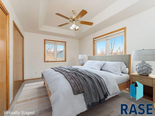 bedroom with a raised ceiling, multiple windows, and ceiling fan