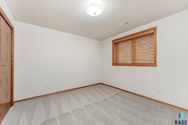 spare room featuring baseboards, a textured ceiling, visible vents, and carpet flooring