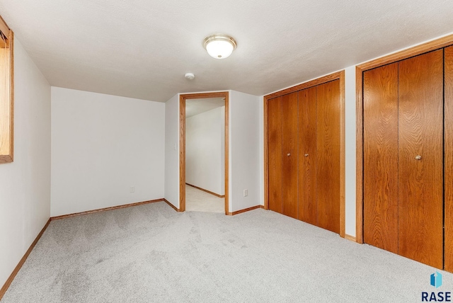 unfurnished bedroom with light carpet, a textured ceiling, multiple closets, and baseboards