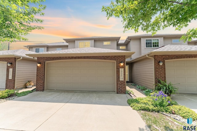 view of front facade featuring an attached garage, driveway, a shingled roof, and brick siding