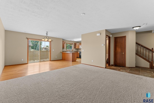 unfurnished living room featuring visible vents, light colored carpet, stairway, a textured ceiling, and a notable chandelier