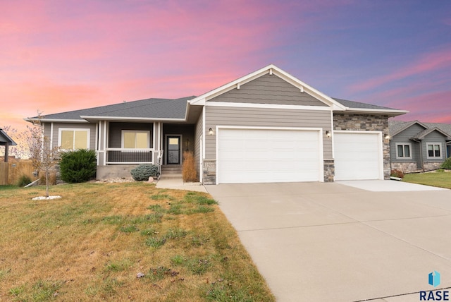 view of front of home featuring a porch, a garage, a yard, stone siding, and driveway