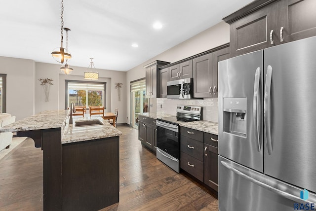 kitchen featuring an island with sink, appliances with stainless steel finishes, decorative light fixtures, a sink, and backsplash