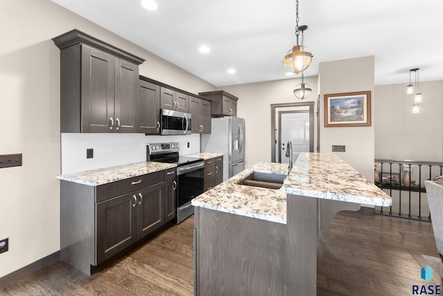 kitchen featuring a kitchen island with sink, appliances with stainless steel finishes, a sink, and decorative light fixtures