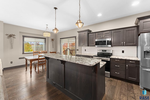 kitchen featuring a breakfast bar, decorative light fixtures, stainless steel appliances, a kitchen island with sink, and dark brown cabinetry