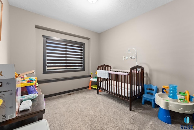 bedroom with a crib, a textured ceiling, baseboards, and carpet flooring