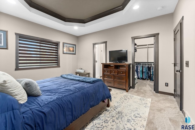 bedroom featuring light carpet, baseboards, a spacious closet, a tray ceiling, and crown molding