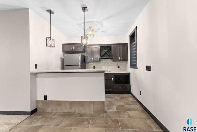 kitchen with decorative backsplash, freestanding refrigerator, hanging light fixtures, light countertops, and a sink