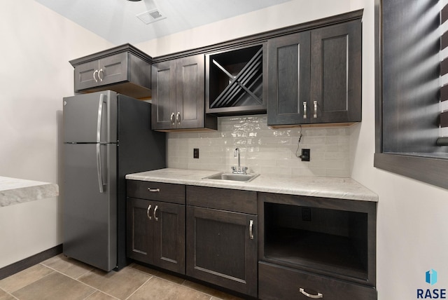 kitchen featuring dark brown cabinets, a sink, freestanding refrigerator, and decorative backsplash