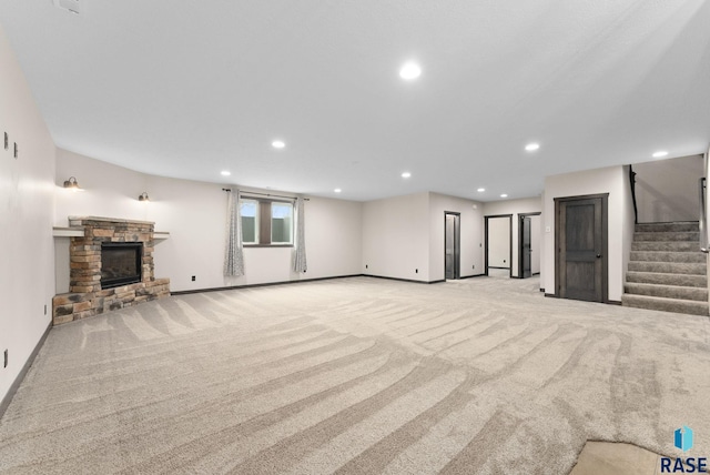 unfurnished living room with recessed lighting, stairway, light carpet, a stone fireplace, and baseboards