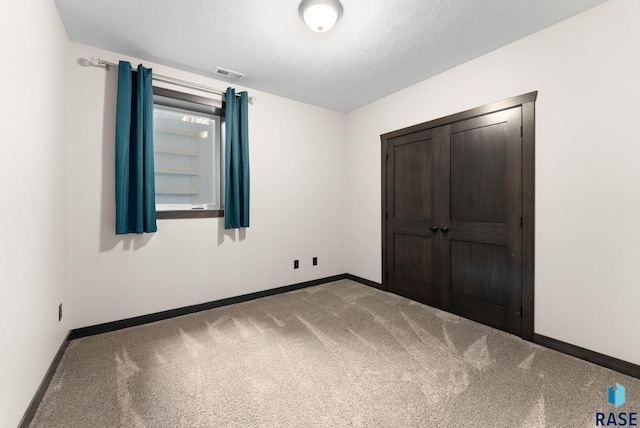 unfurnished bedroom featuring a textured ceiling, carpet flooring, visible vents, baseboards, and a closet