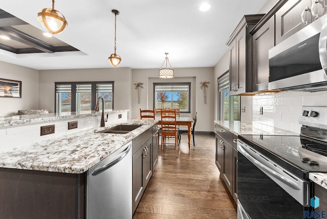 kitchen with dark brown cabinetry, dark wood-type flooring, decorative light fixtures, stainless steel appliances, and a large island with sink