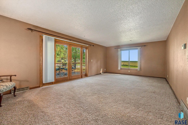 carpeted spare room with visible vents, a textured ceiling, and baseboards