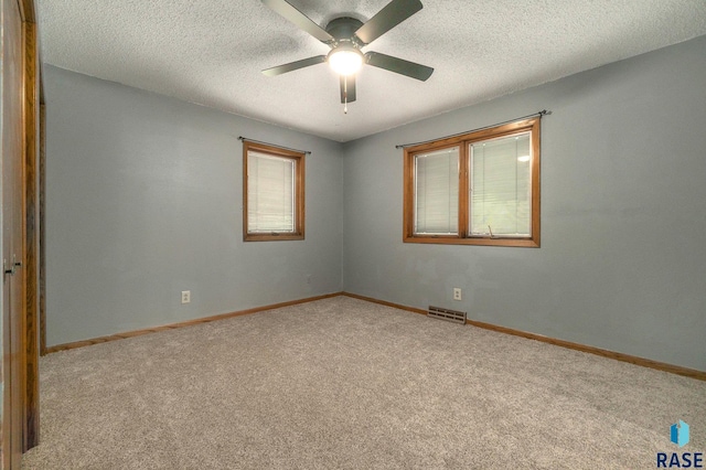 empty room featuring visible vents, a ceiling fan, light carpet, a textured ceiling, and baseboards