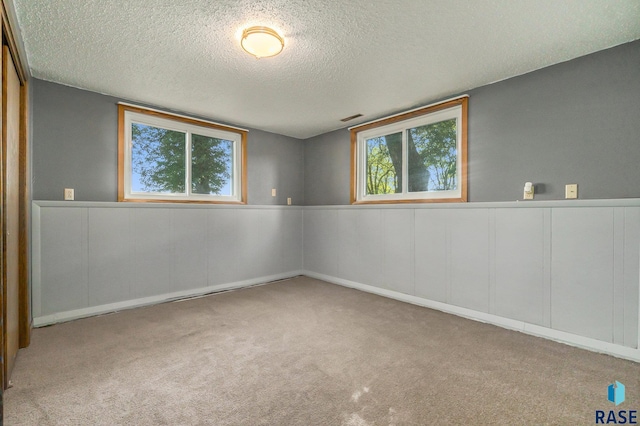 spare room with a textured ceiling, a healthy amount of sunlight, visible vents, and light colored carpet