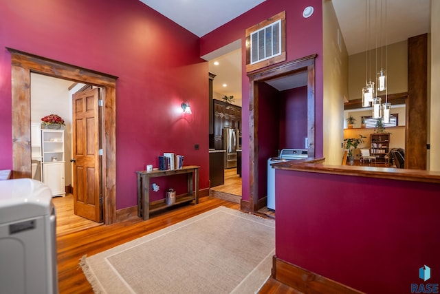 bar featuring visible vents, wood finished floors, independent washer and dryer, hanging light fixtures, and freestanding refrigerator