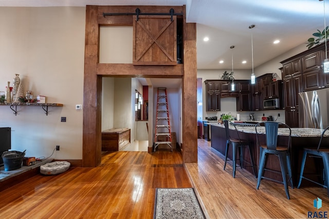 kitchen with light stone counters, a breakfast bar area, decorative light fixtures, stainless steel appliances, and dark brown cabinets