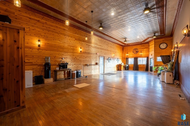 unfurnished living room with ceiling fan, wooden walls, a high ceiling, wood finished floors, and an ornate ceiling