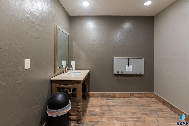 bathroom with baseboards, a textured wall, vanity, wood finish floors, and recessed lighting