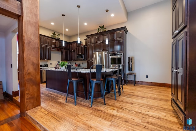kitchen with a center island with sink, a kitchen breakfast bar, decorative light fixtures, light stone countertops, and stainless steel appliances