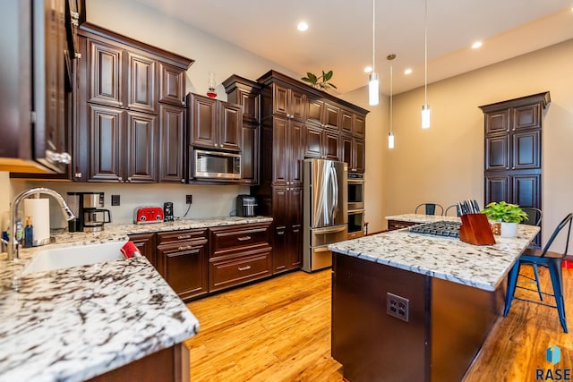 kitchen with a center island, decorative light fixtures, a breakfast bar area, appliances with stainless steel finishes, and a sink